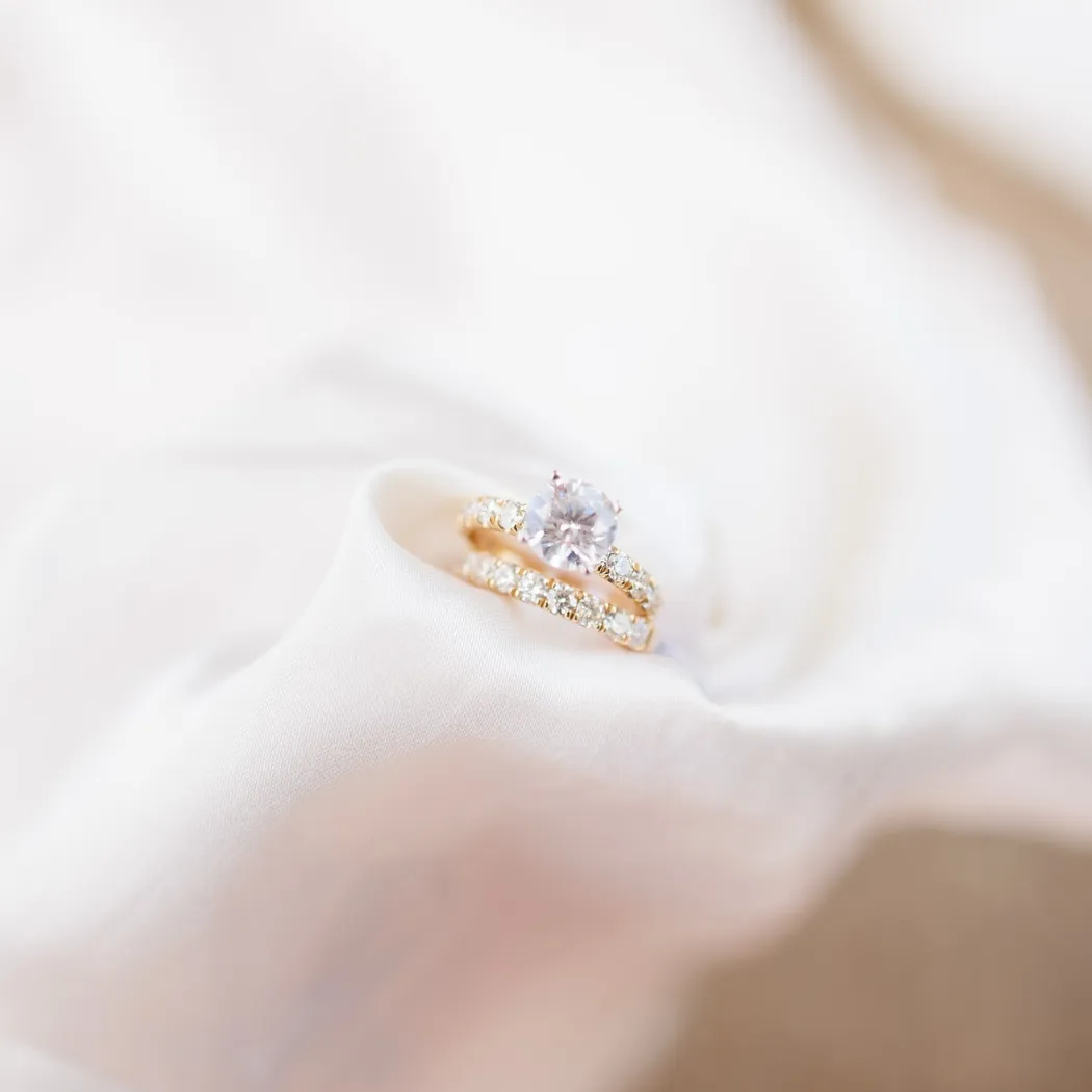 Elegant gold engagement and wedding rings on soft fabric, showcasing a sparkling center stone and delicate detailing.