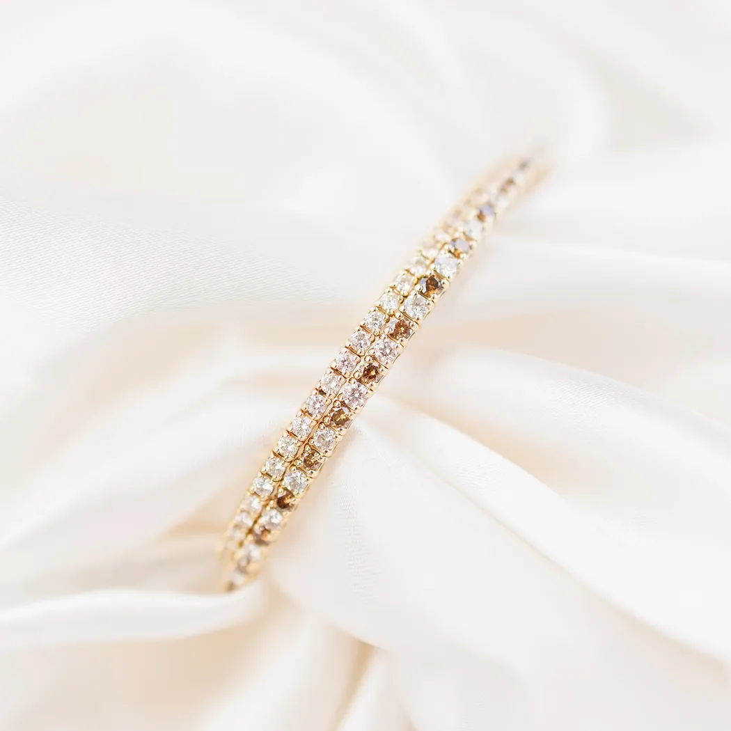 Elegant gold bracelet adorned with sparkling diamonds on soft white fabric background.