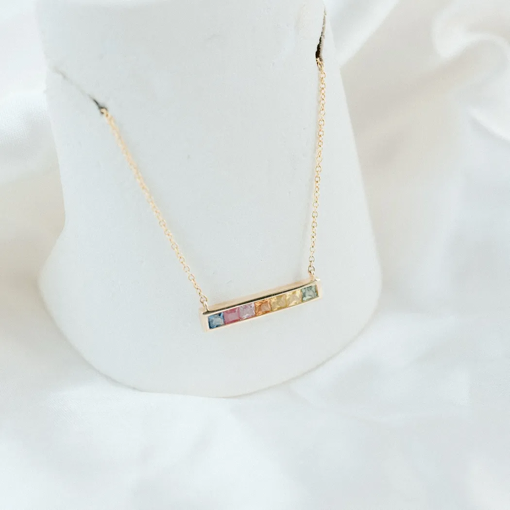Gold bar necklace with colorful gemstones displayed on a white bust, showcasing fine jewelry from Barnes Jewelers.