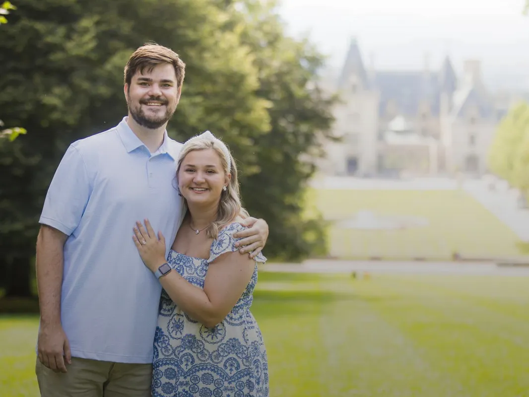 Mike and Carol pose happily together outdoors with a mansion in the background, showcasing their engagement.