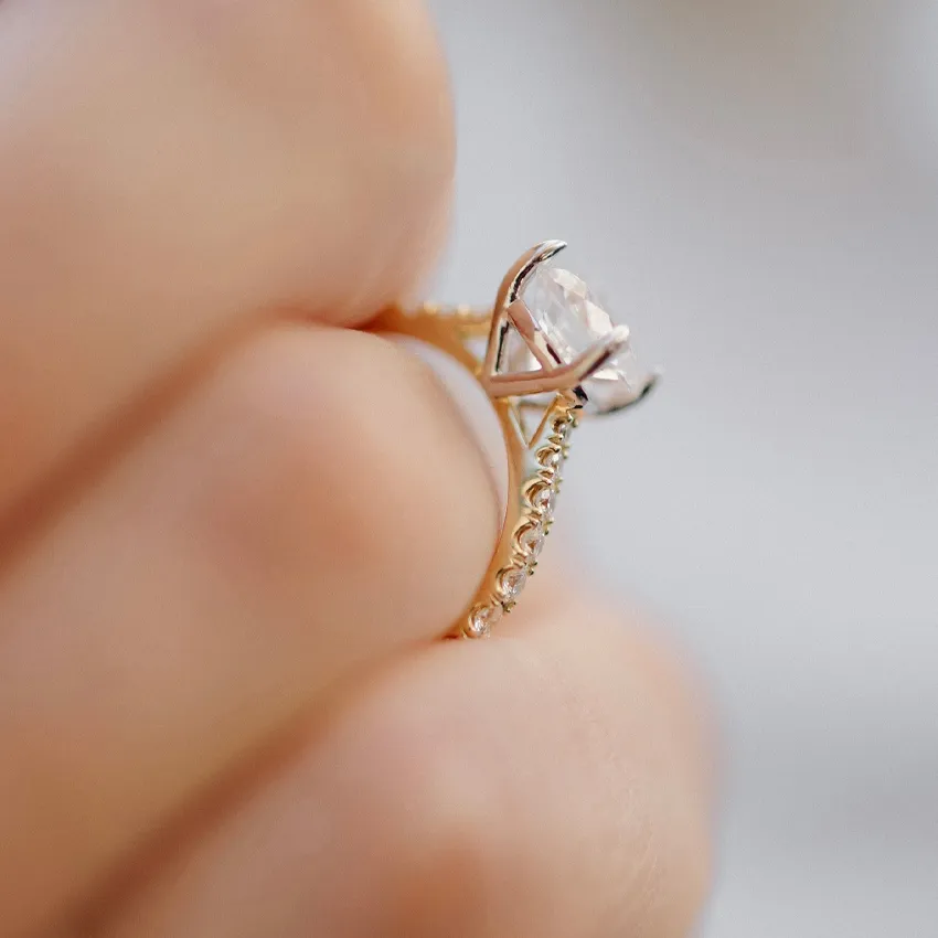 Elegant engagement ring held in hand, featuring a sparkling center stone and intricate band design.