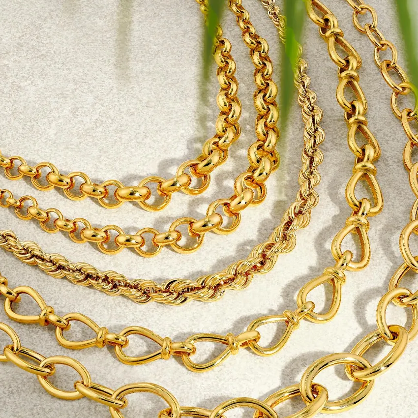 Close-up of layered gold chains on a light surface, showcasing various styles and textures.