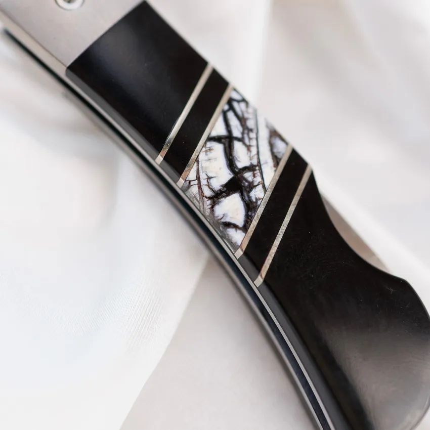 Close-up of a knife handle featuring black and white inlay design, showcasing craftsmanship.