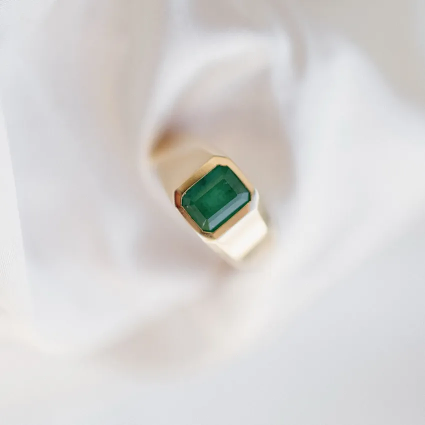Emerald-cut green gemstone ring set in gold, displayed on soft fabric.