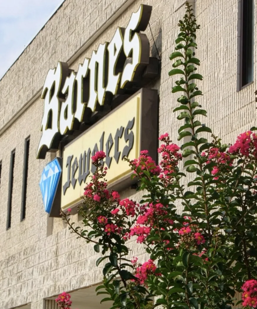 Barnes Jewelers sign with pink flowers in front, located in Goldsboro, showcasing fine jewelry and engagement rings.