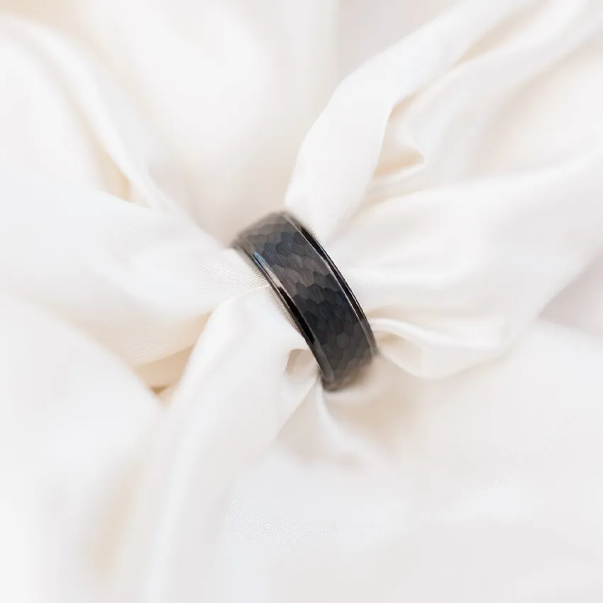 Black hexagonal wedding band resting on white fabric, showcasing its unique texture.