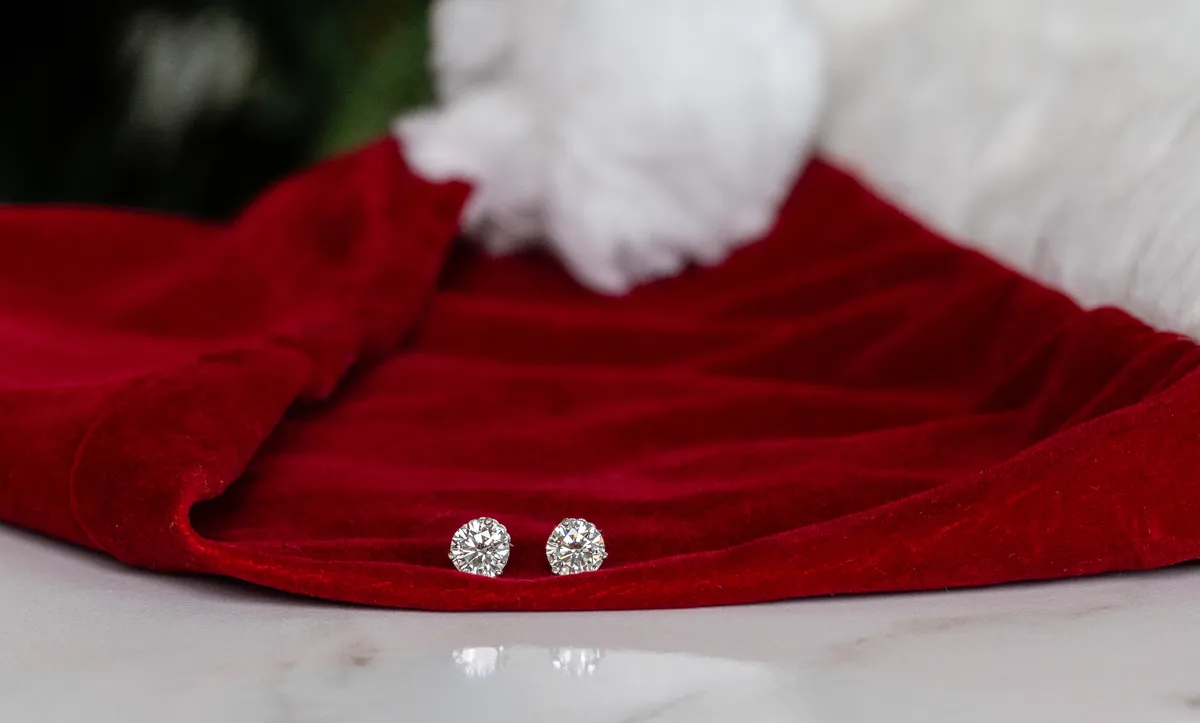 A pair of diamond stud earrings resting on the white fur trim of a red Santa hat