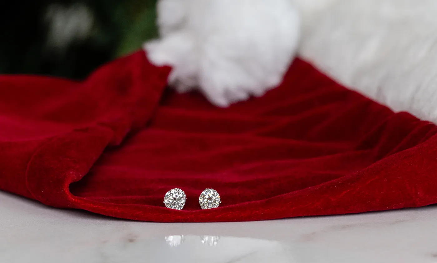 A pair of diamond stud earrings resting on the white fur trim of a red Santa hat