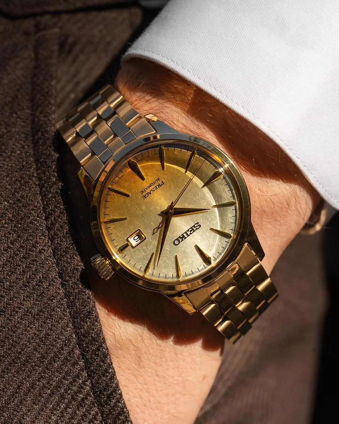 A man in a suit wearing a gold-dial Seiko watch