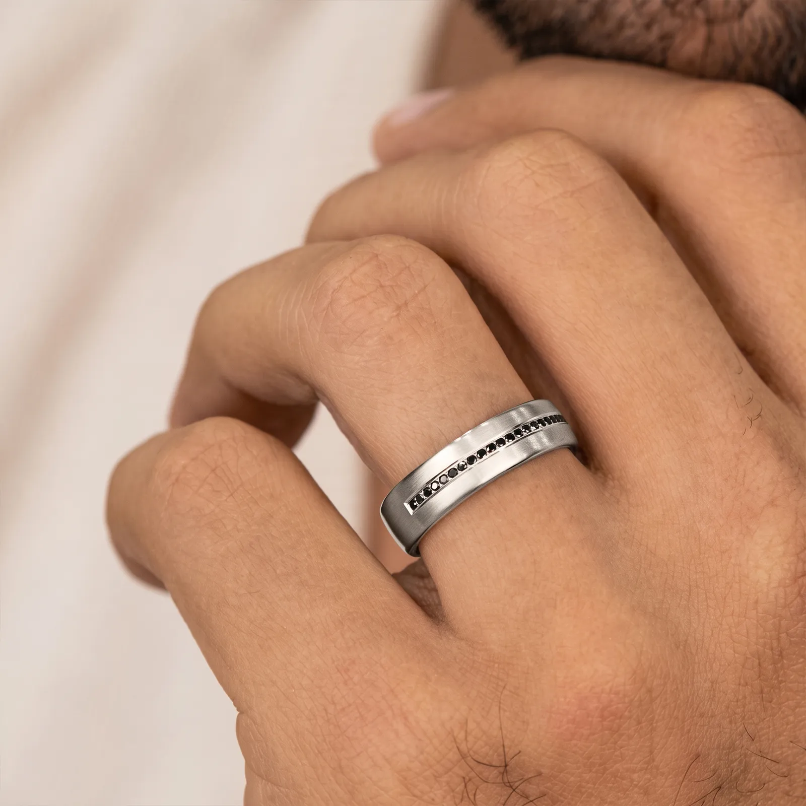 A hand wearing a silver ring with black stones inlaid in a line.
