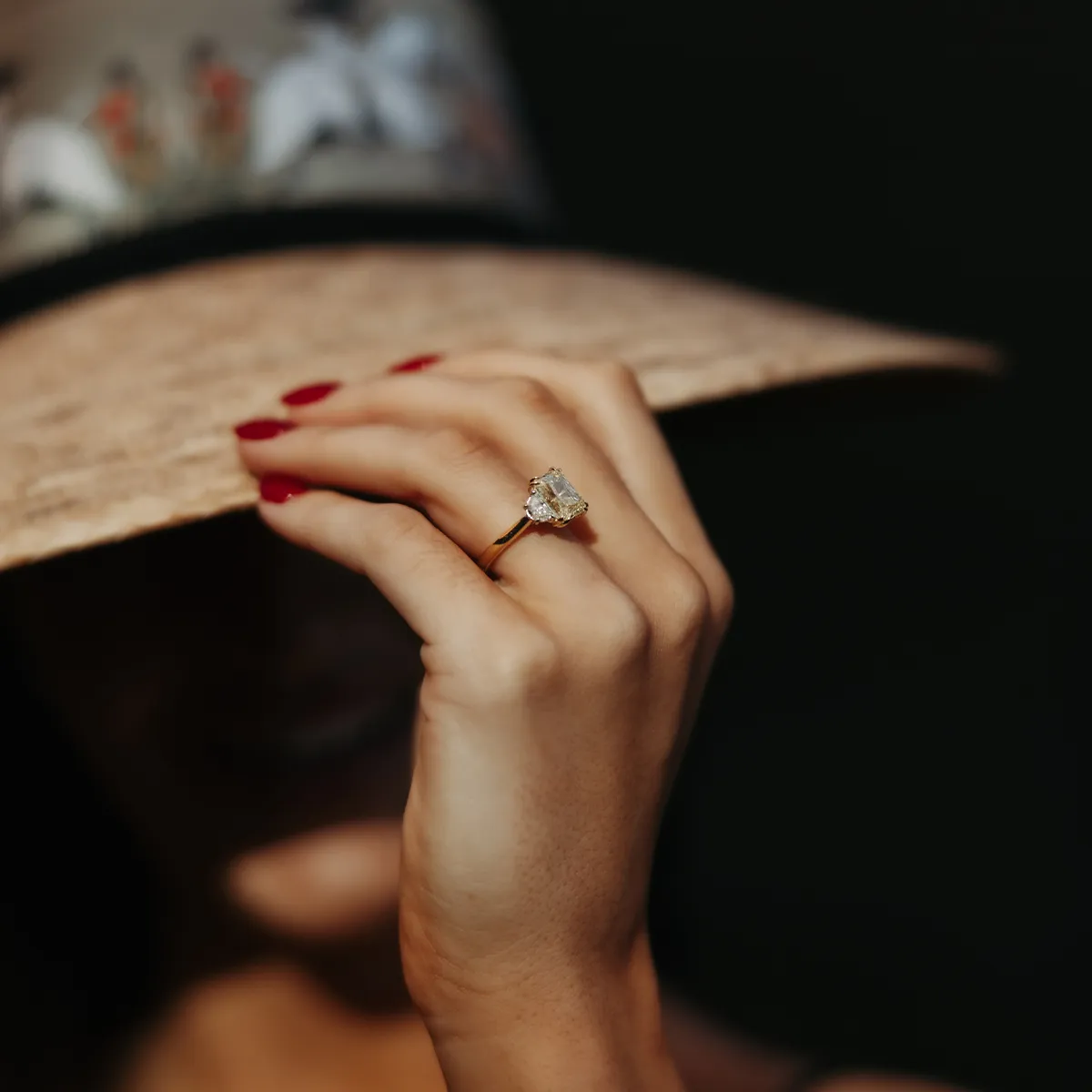 A person with red nails wearing a large diamond ring and a wide-brimmed hat.