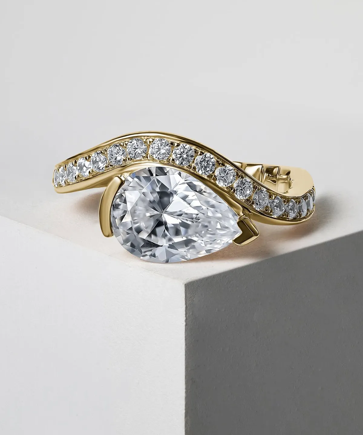 A pear-shaped diamond ring with a gold band adorned with smaller diamonds.
