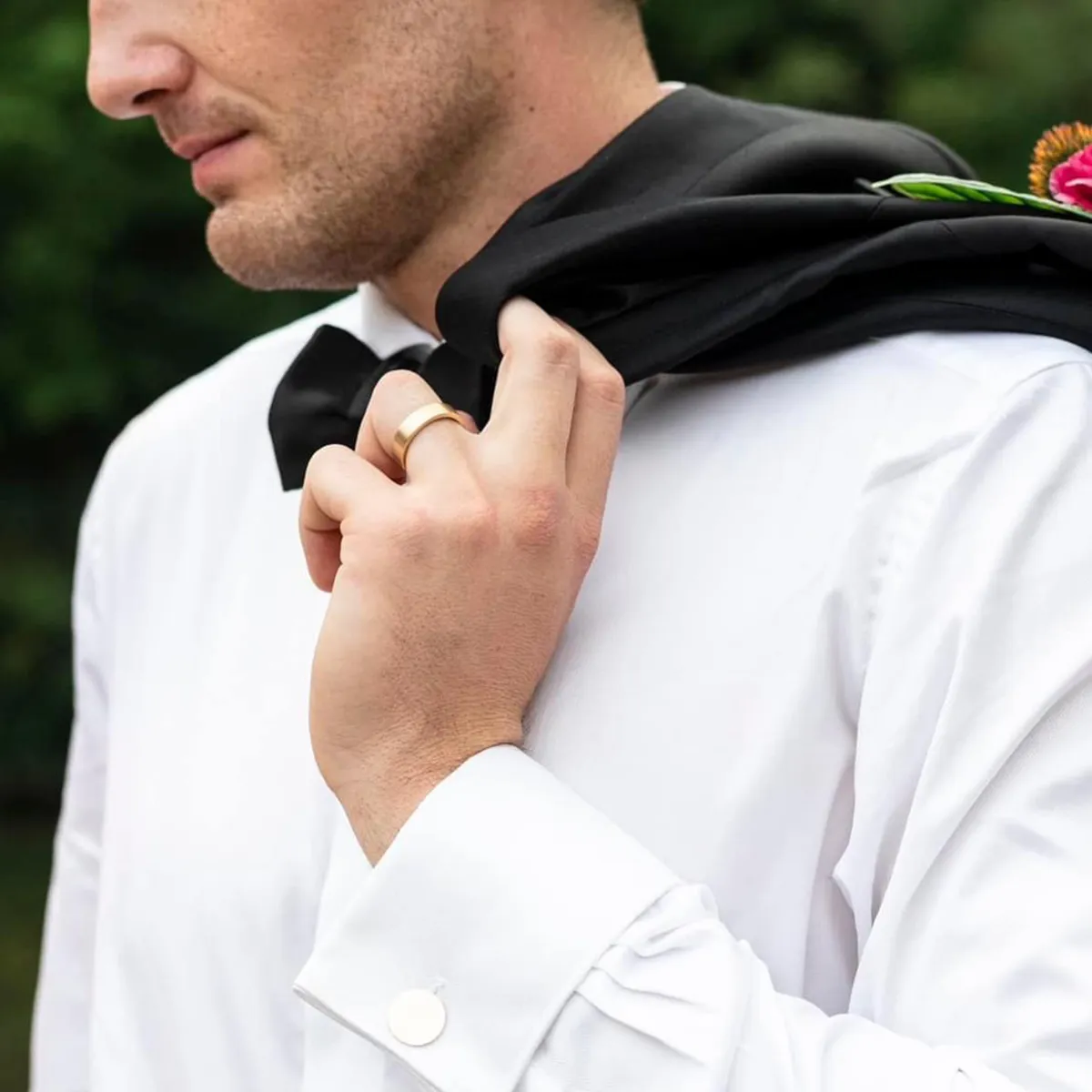 A man in a white shirt with a black jacket over his shoulder, wearing a gold ring.