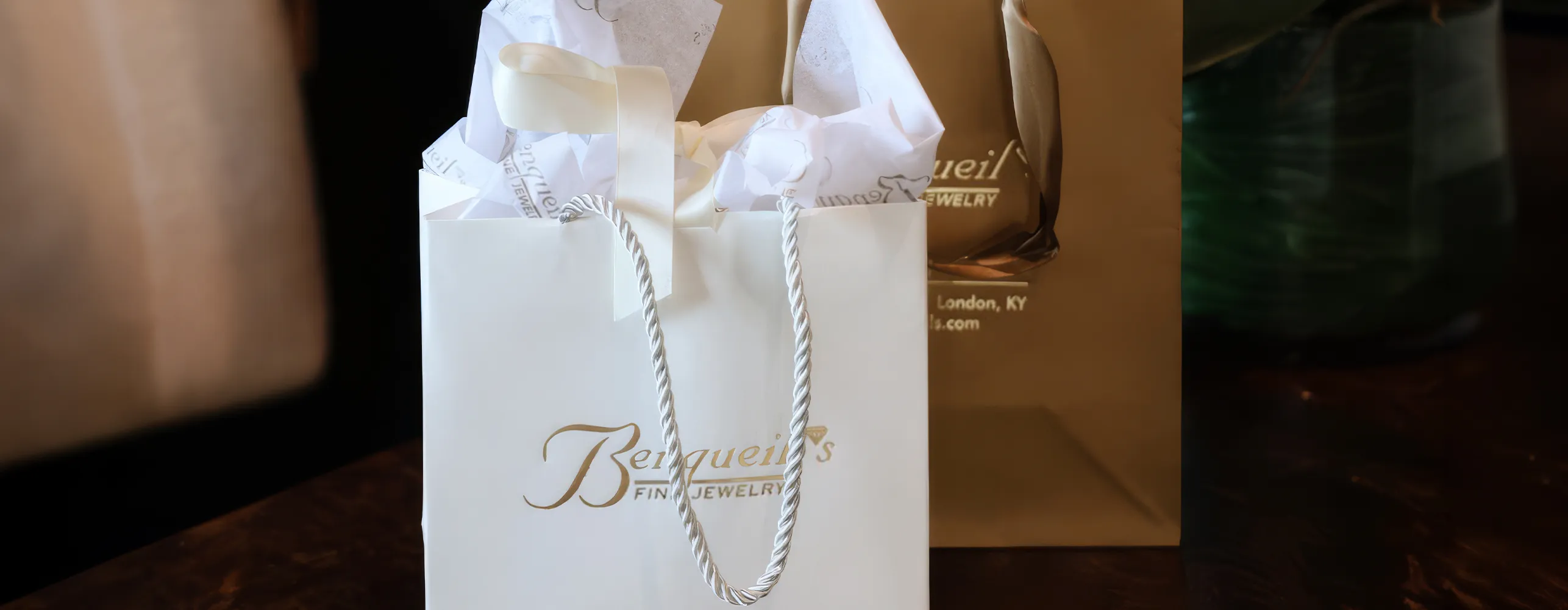 A white gift bag with gold lettering and tissue paper, next to a brown bag.