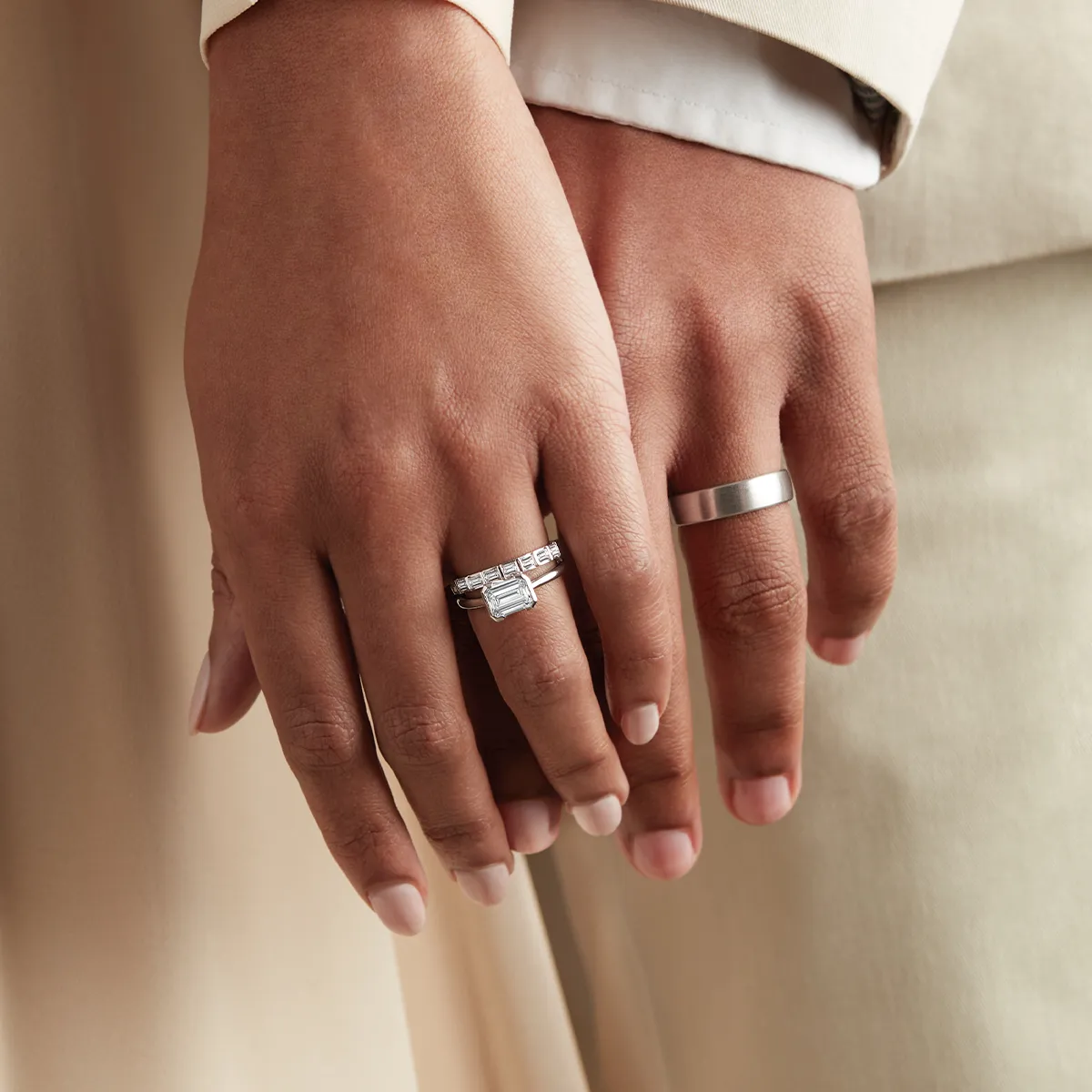 Two hands with wedding rings; one with a diamond ring, the other with a plain band.