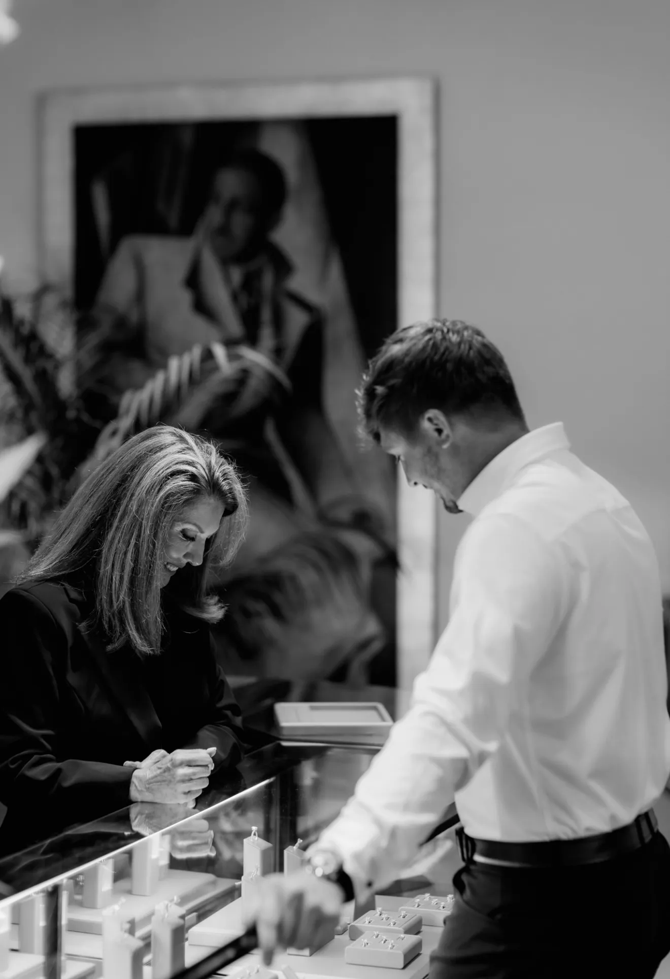 A man and woman smiling at each other across a jewelry store counter.