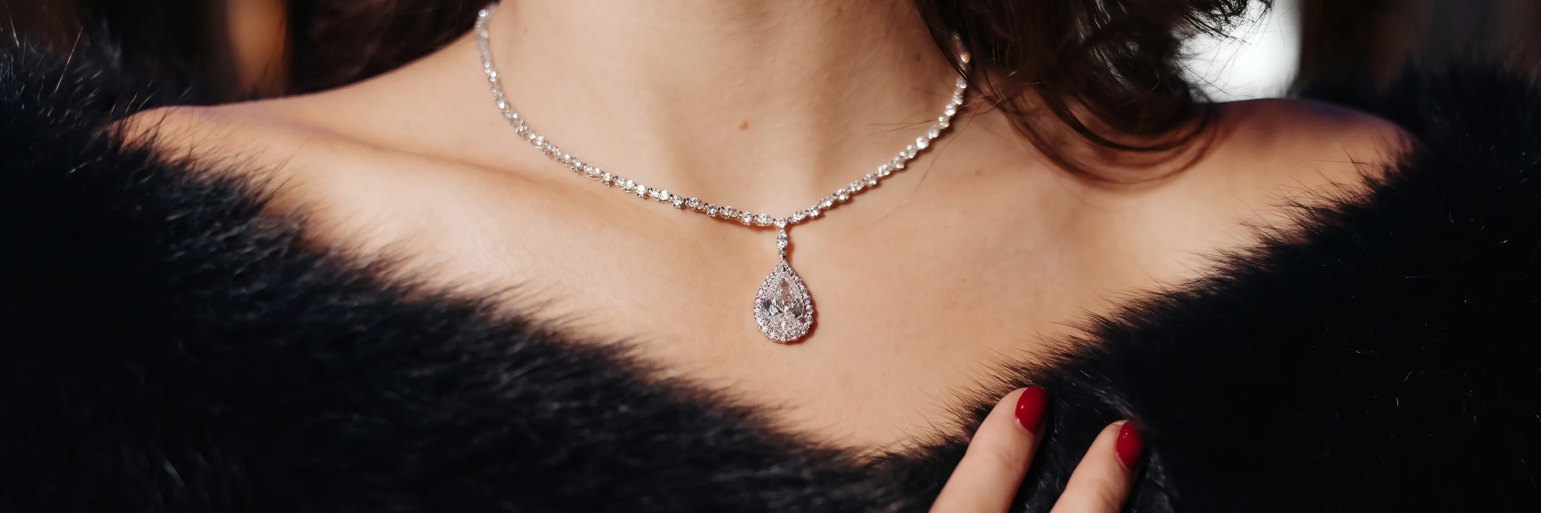 A woman wearing a diamond necklace with a teardrop pendant, dressed in a black fur garment.