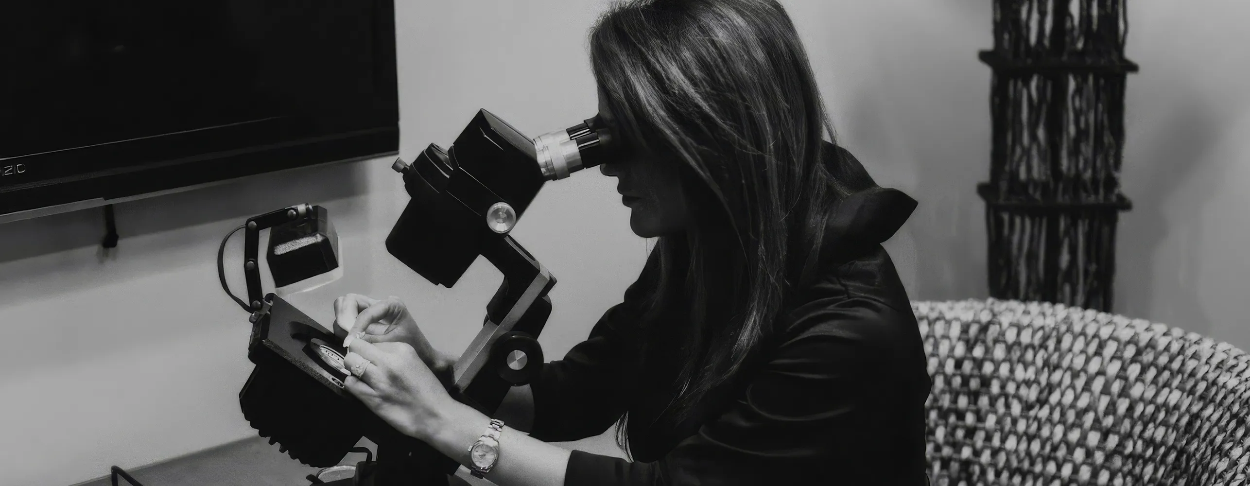 A person examining jewelry under a microscope in a black and white image.