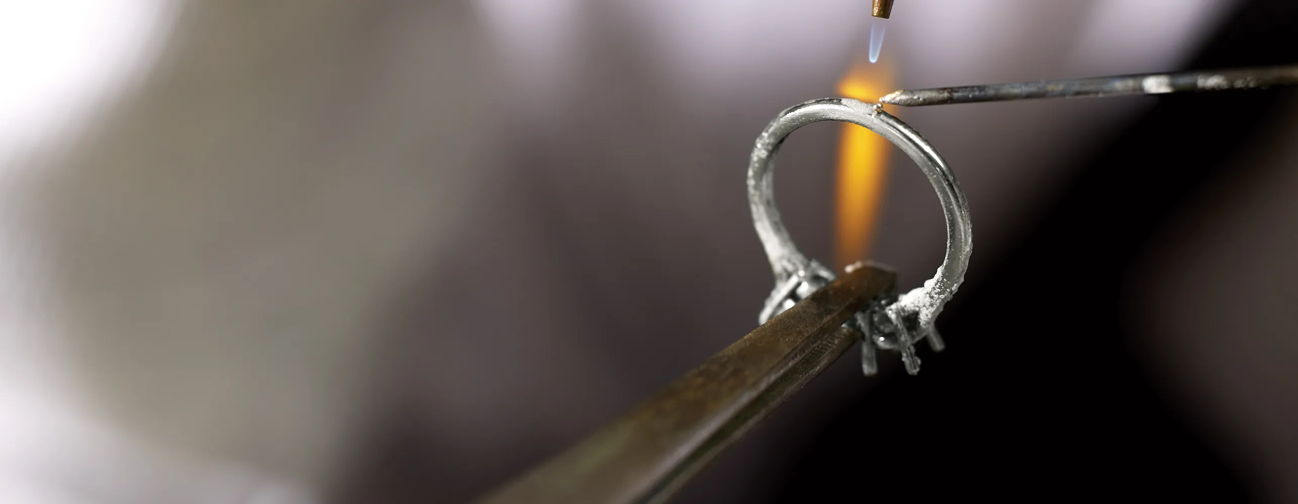 A jeweler uses a flame torch to work on a metal ring held by tweezers.