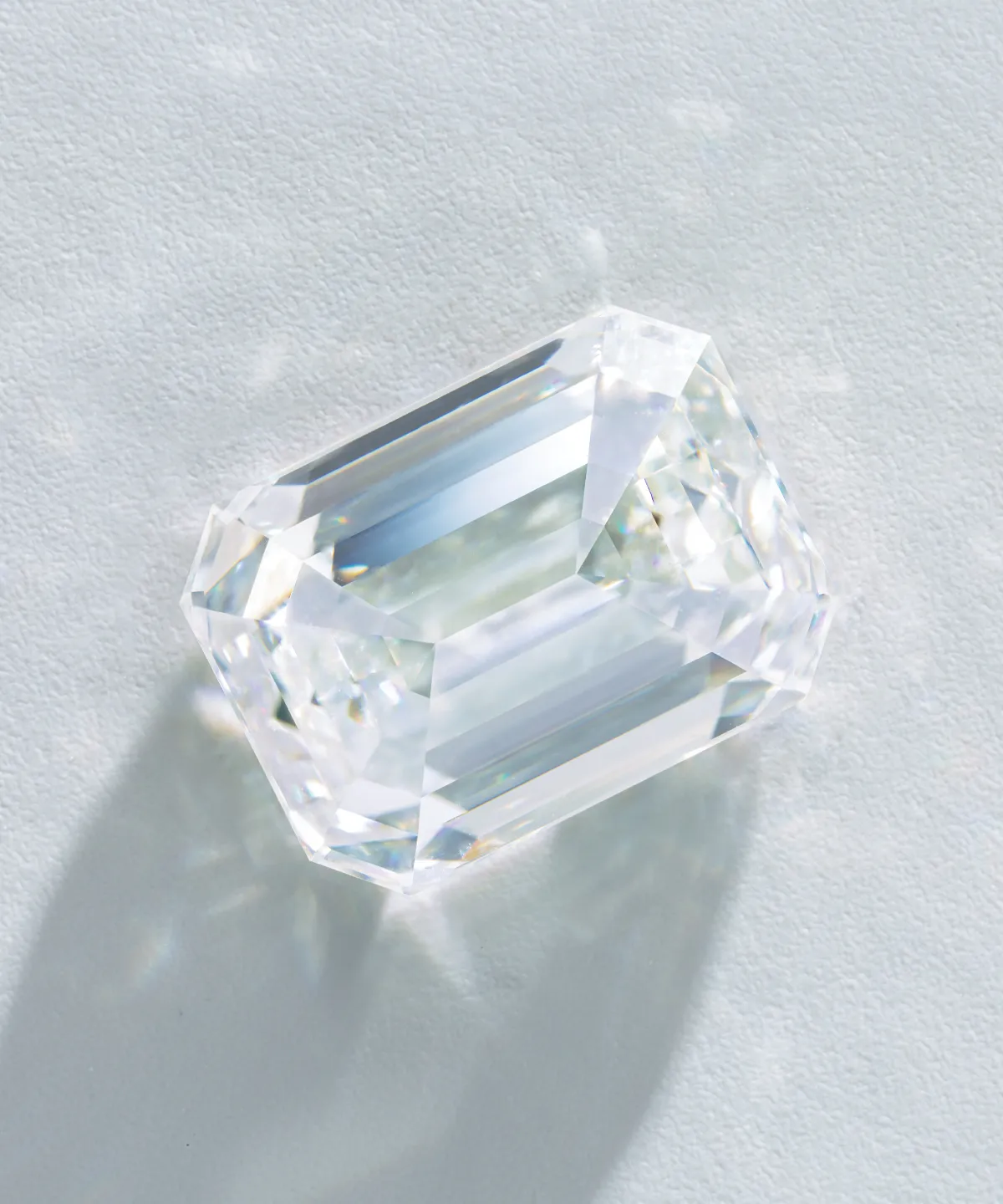 A radiant, rectangular-cut diamond on a light surface, casting a shadow.