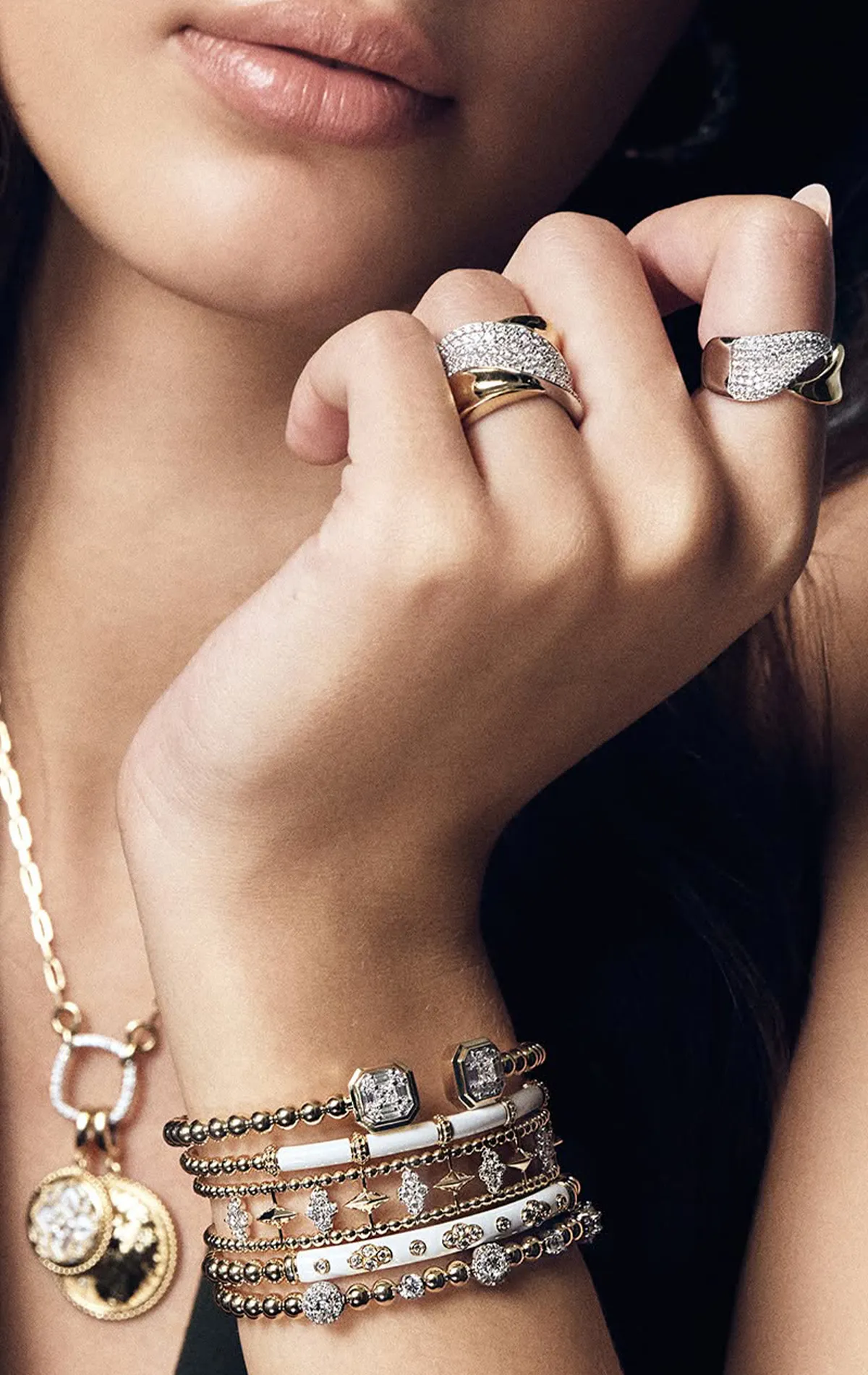 Close-up of a woman's hand adorned with gold and diamond rings, bracelets, and a necklace.