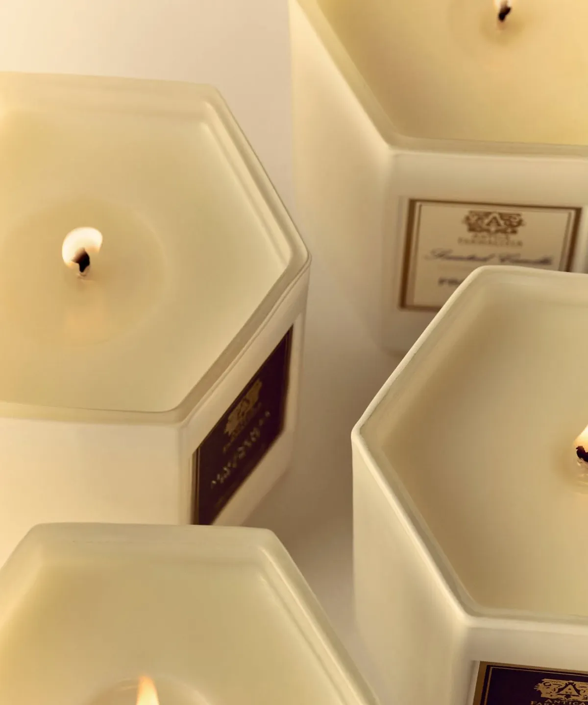 Hexagonal candles with lit wicks in cream-colored containers.