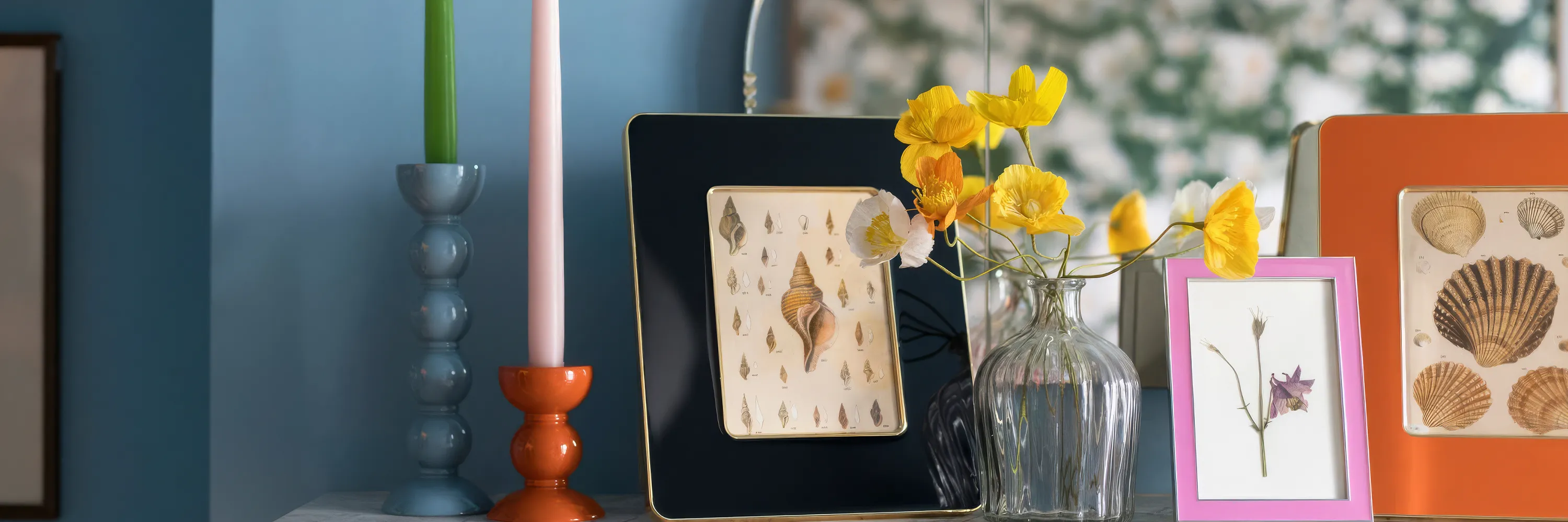 Colorful frames, candles, and flowers on a blue shelf.
