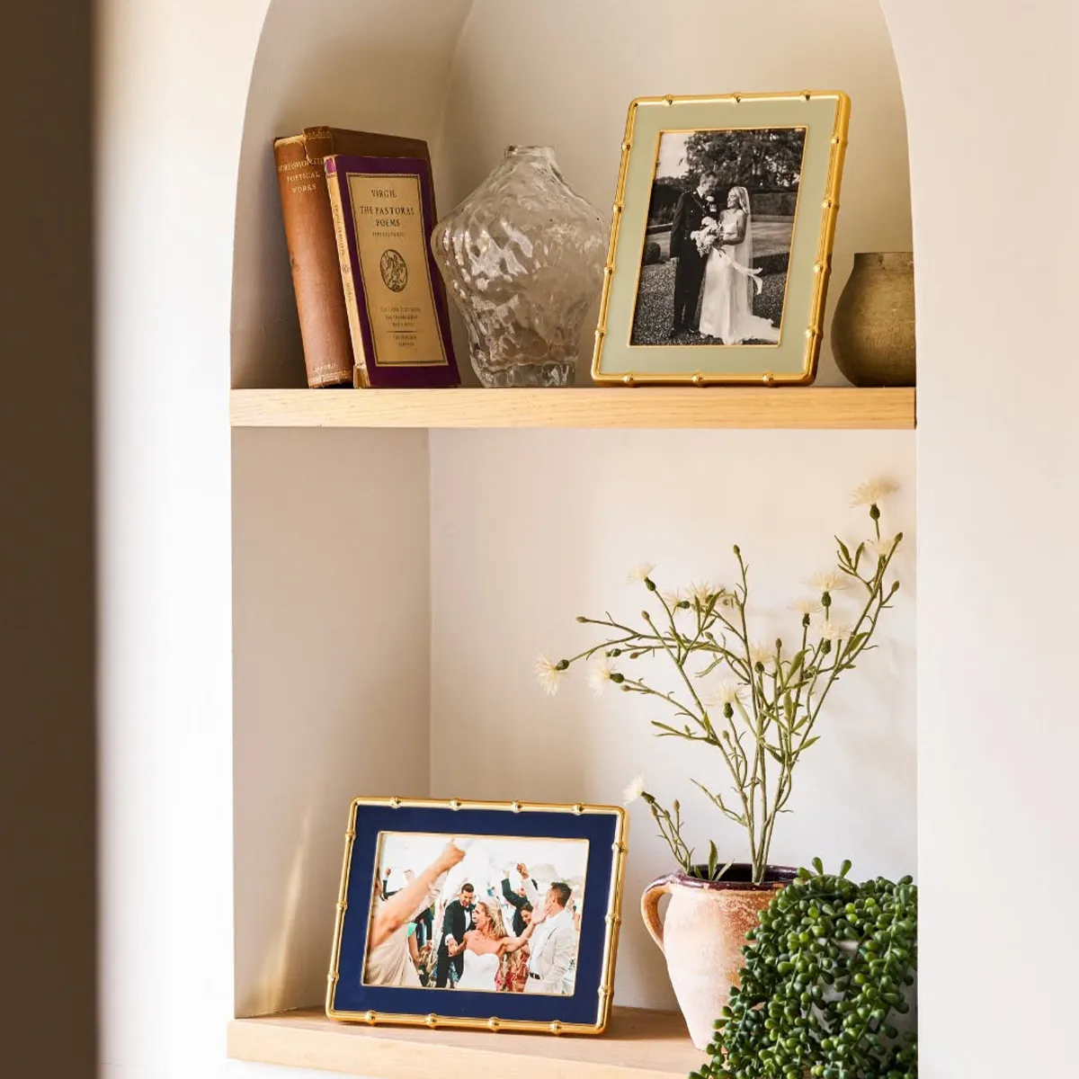 Wooden shelf with framed photos, books, a vase, and a potted plant.