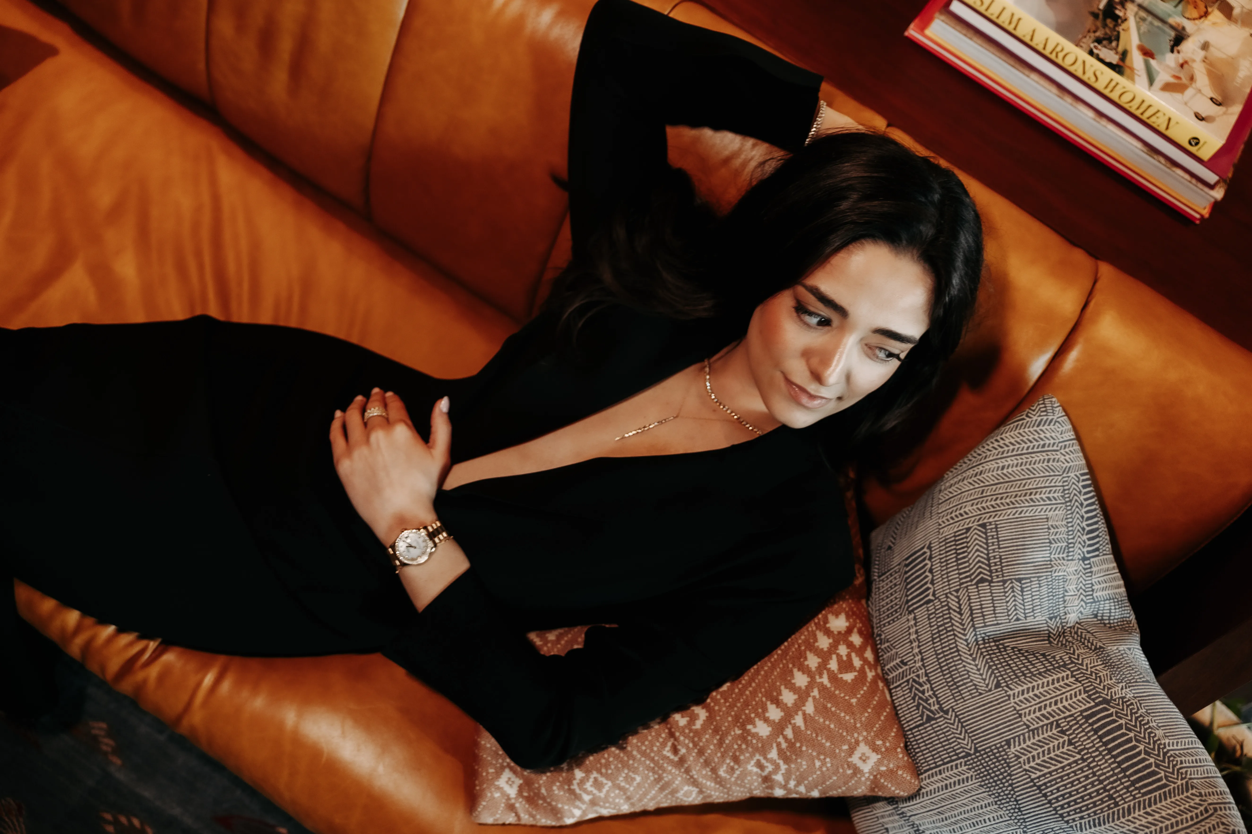 A person wearing a blue gemstone necklace and ring with manicured hands on their chest.