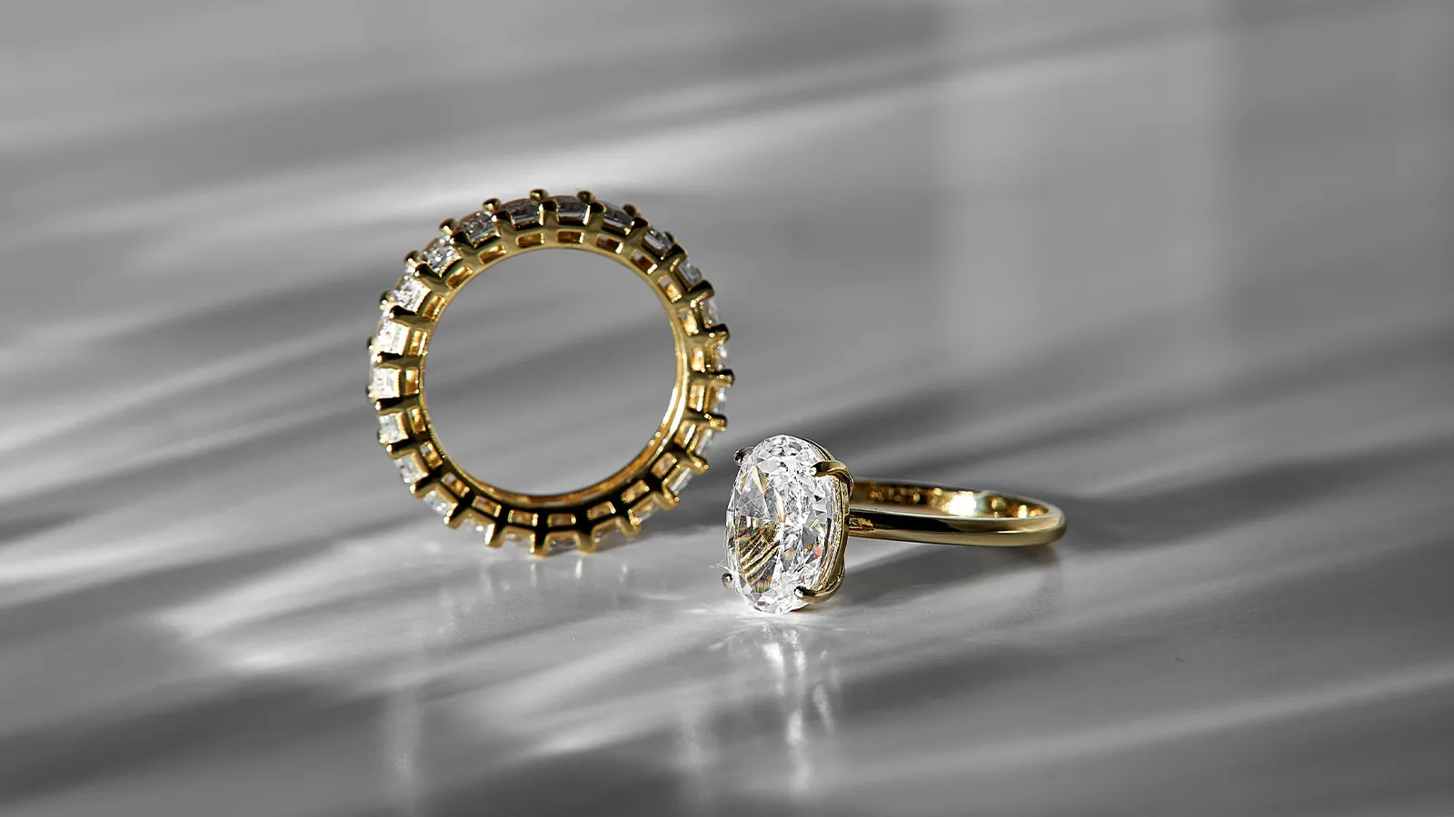 A gold diamond eternity band standing on edge beside a yellow gold ring set with an oval diamond, on soft grey silk