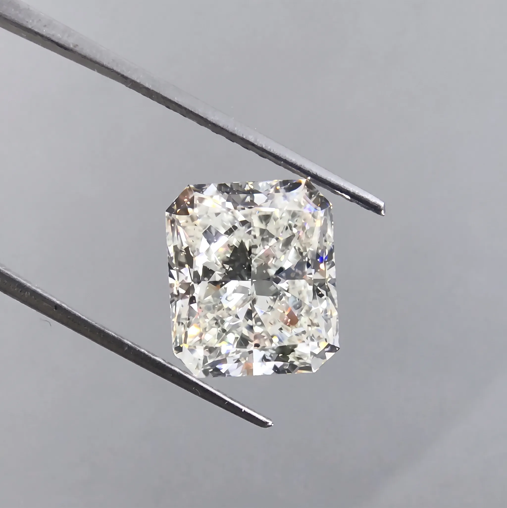 A loose emerald cut diamond held in jeweler's tweezers while its color is examined