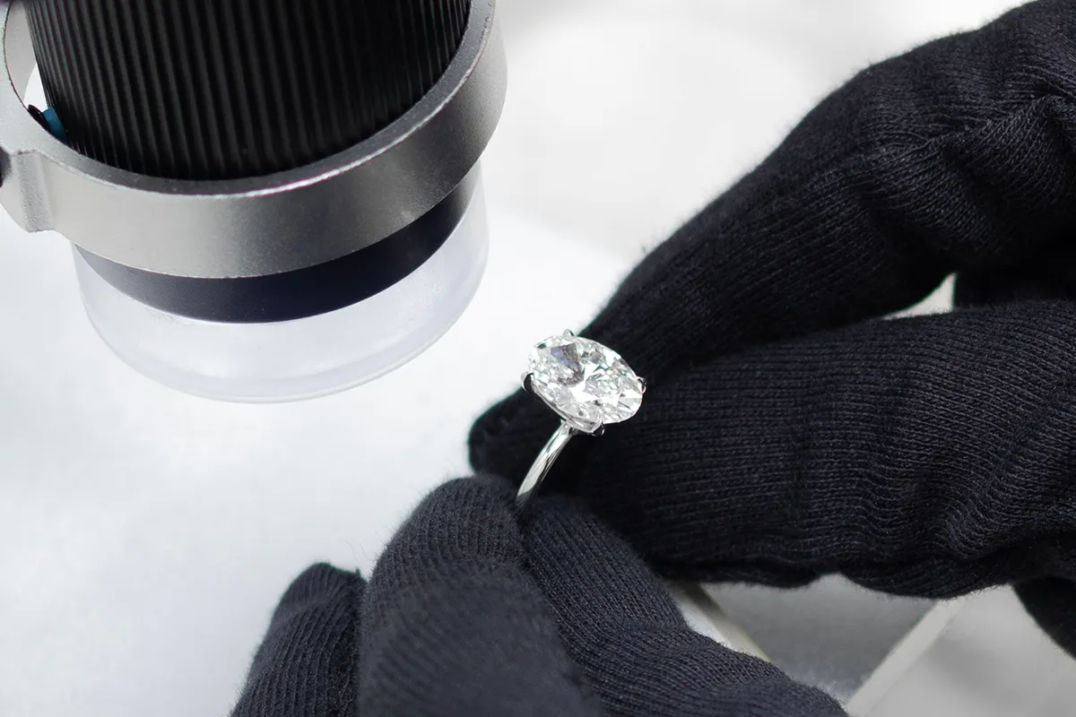 A gloved jeweler holding a diamond ring up to a microscope to inspect the center stone
