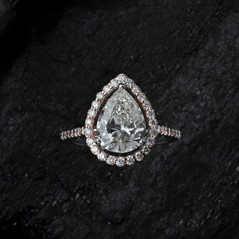 A pear shaped natural diamond engagement ring with a pave set band, photographed on dark stone