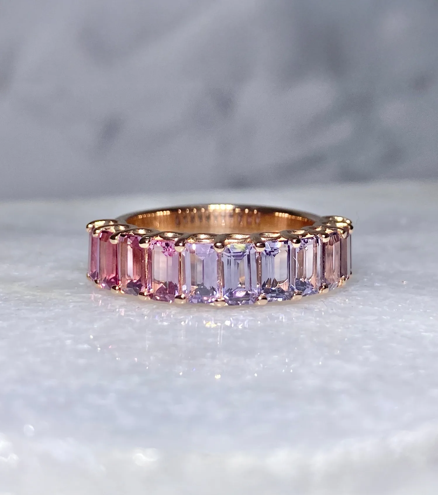 Rose gold ring with alternating pink and purple gemstones, showcasing a vibrant and elegant design.