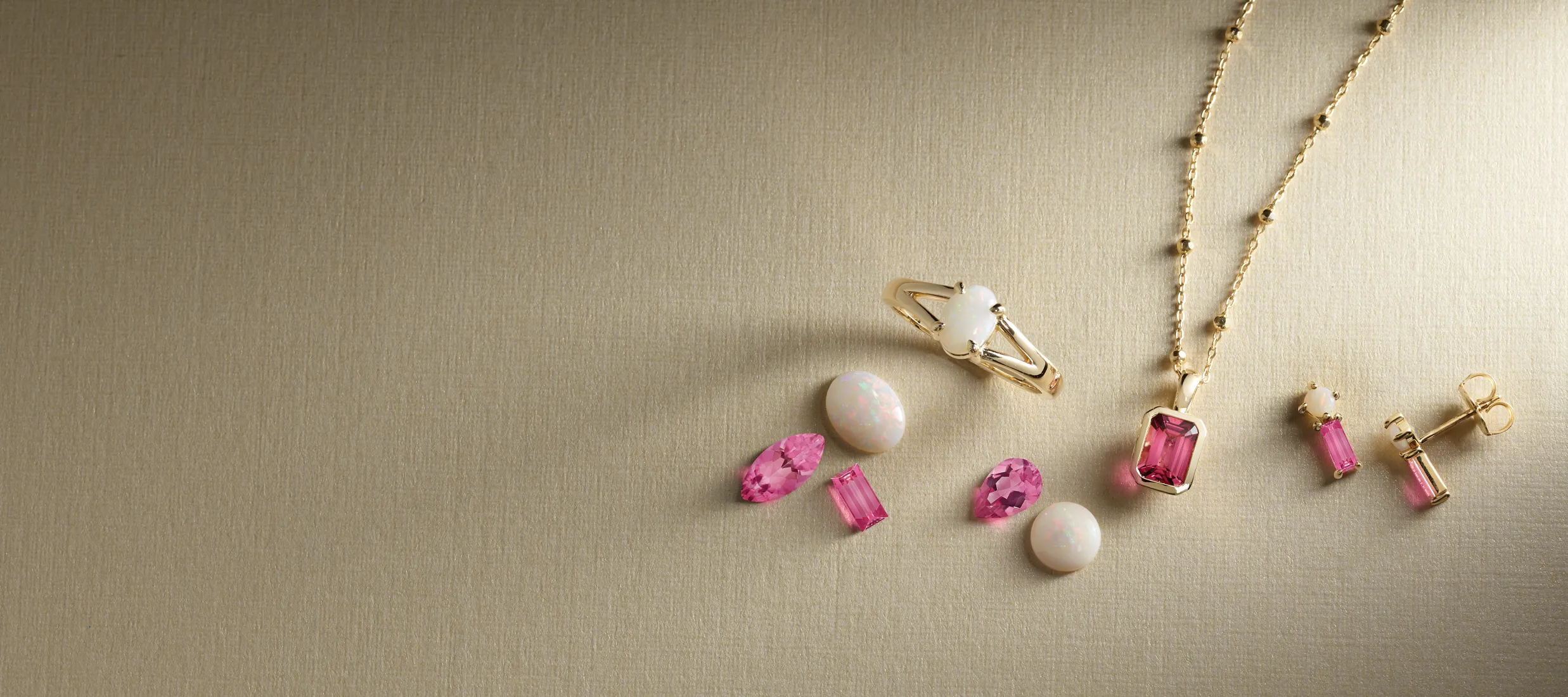 Jewelry display featuring pink gemstones, a gold necklace, and an opal ring. Click to shop gemstone jewelry at Bethany's Jewelry