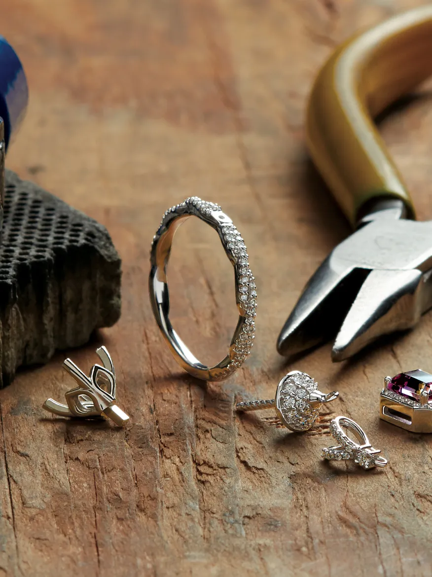 Jewelry tools and pieces including a diamond ring, earrings, and pliers on a wooden surface at Bethany's Jewelry.