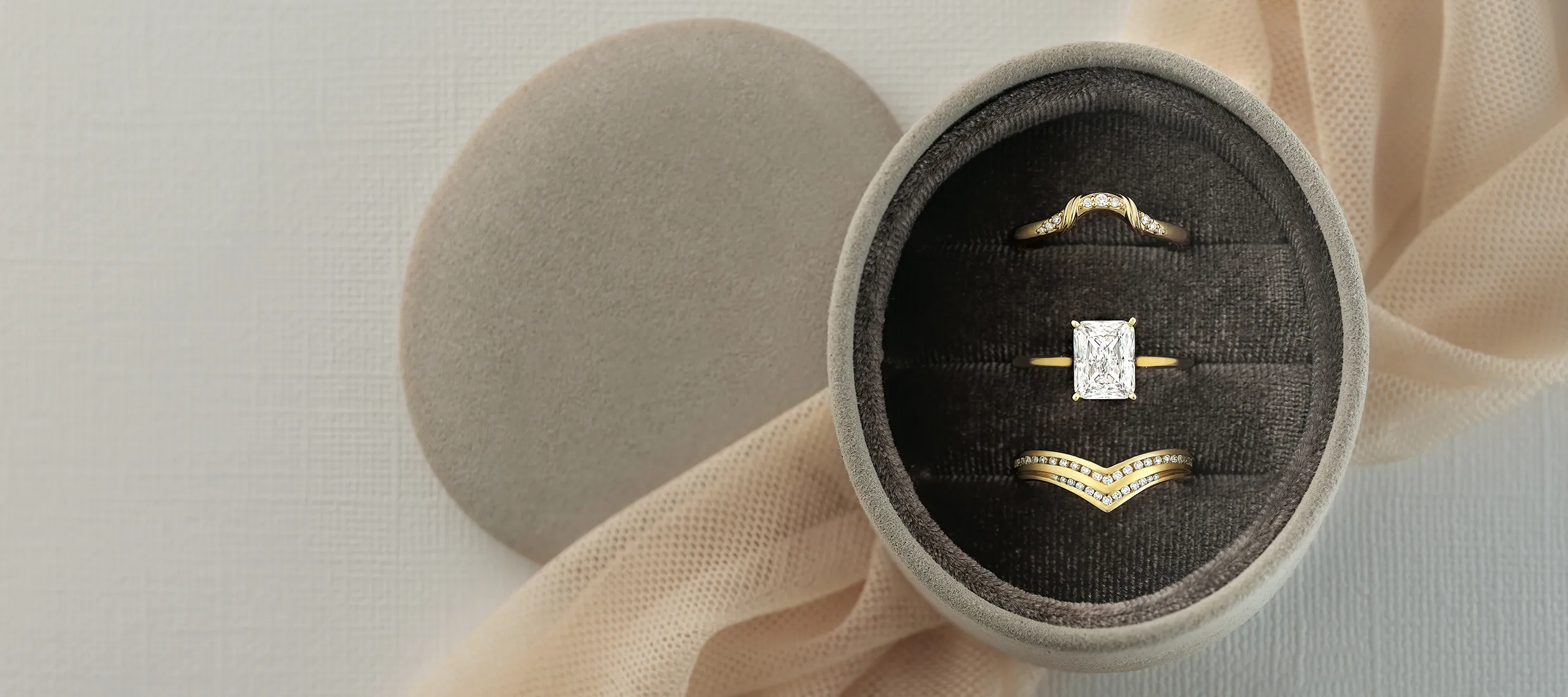 Three elegant gold rings displayed in a soft gray jewelry box, featuring a diamond centerpiece and intricate designs.