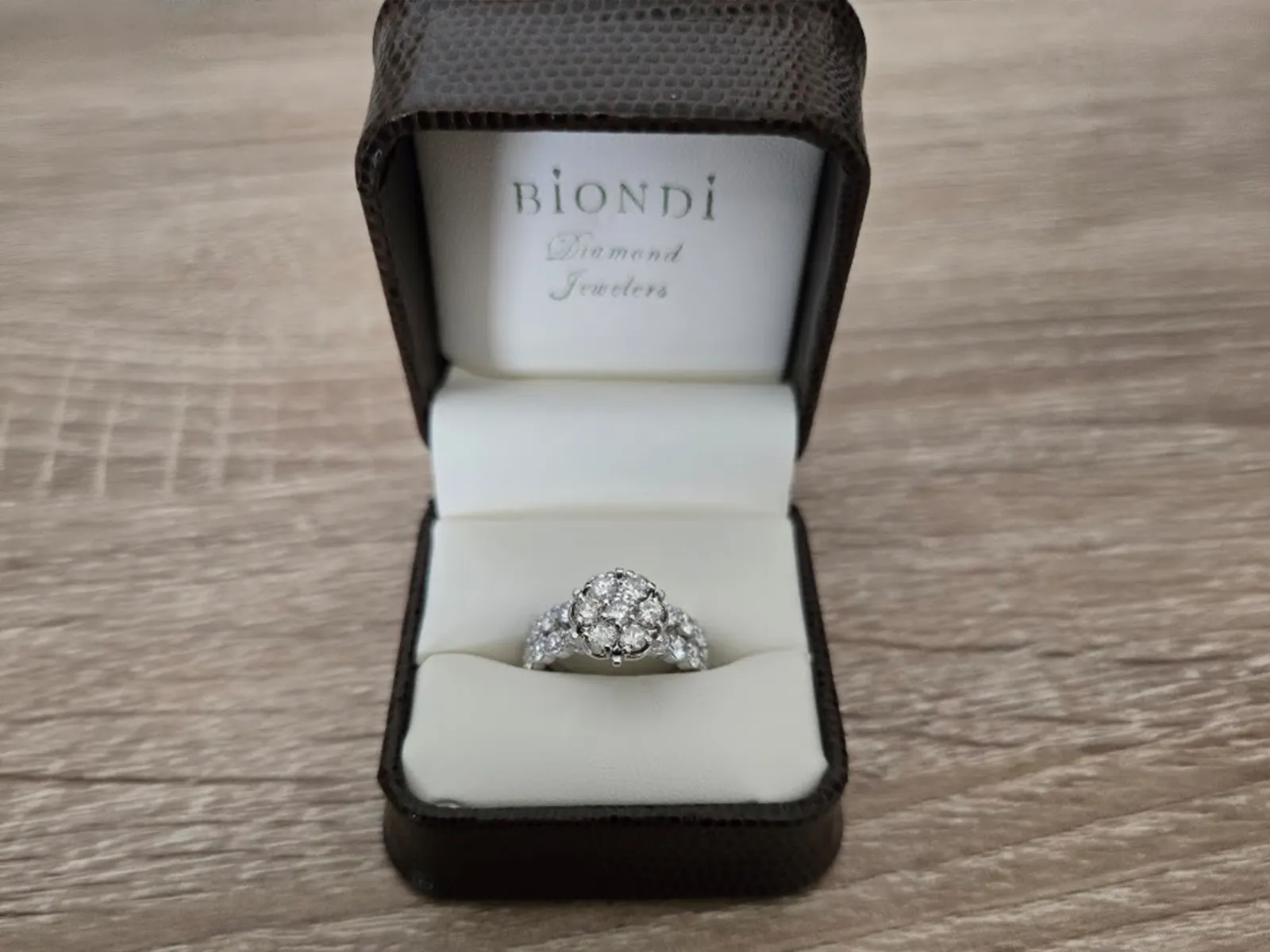 A diamond ring in an open jewelry box on a wooden surface.