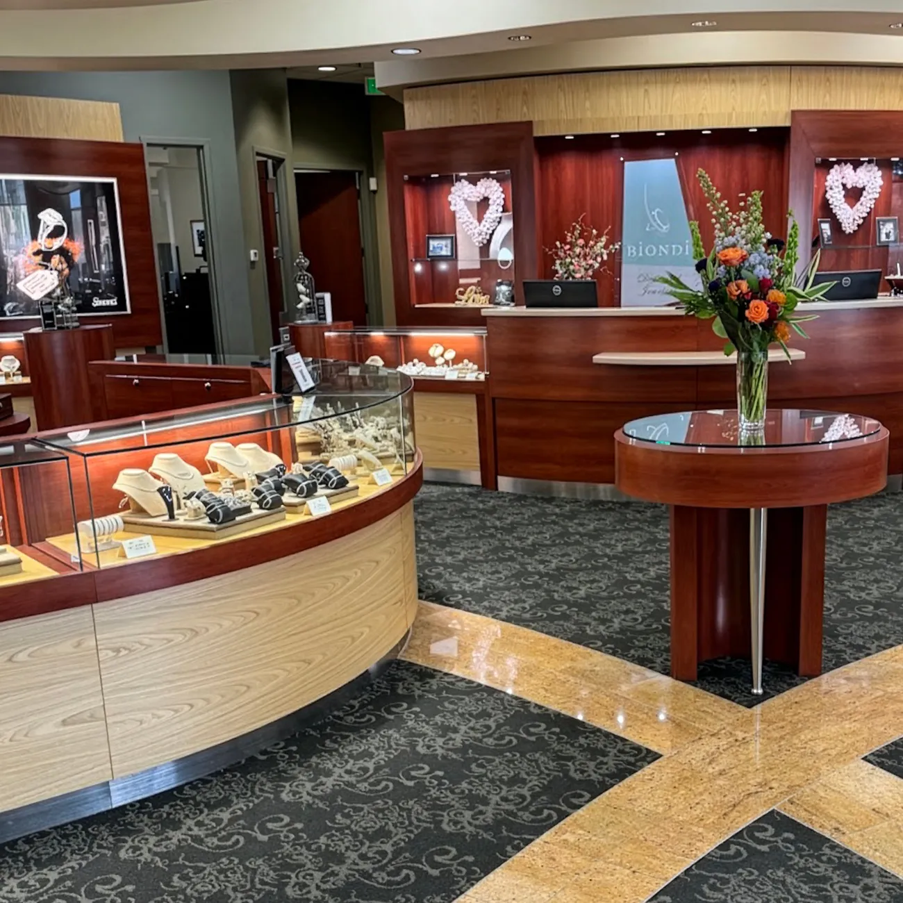 Interior of a jewelry store with display cases, floral arrangement, and elegant decor.