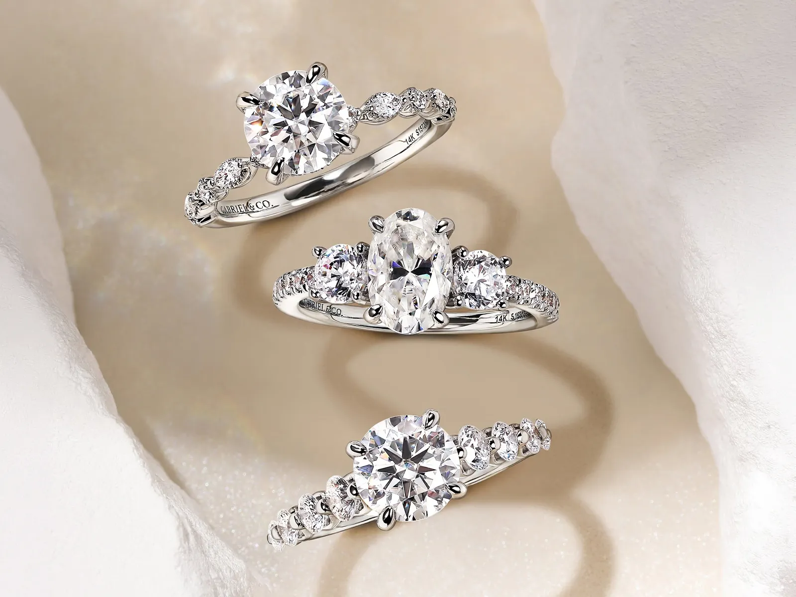 Three elegant diamond engagement rings with intricate band designs on a soft, textured background.