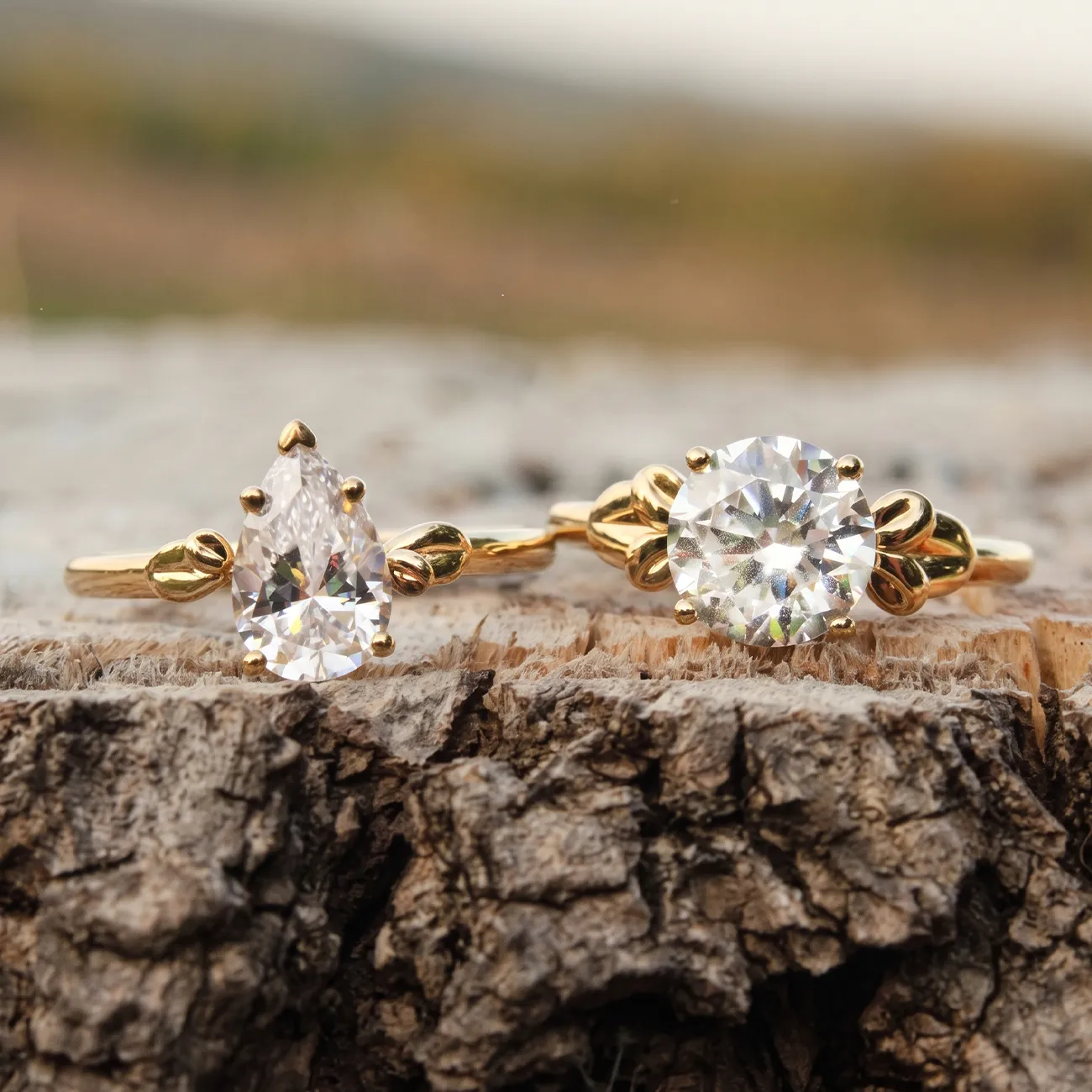 Two gold rings with pear and round-cut diamonds on a textured wooden surface.