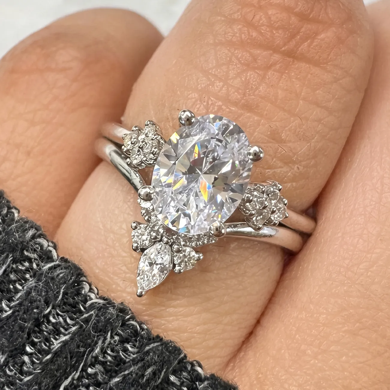A hand wearing a silver engagement ring with a large oval diamond and smaller accent stones.