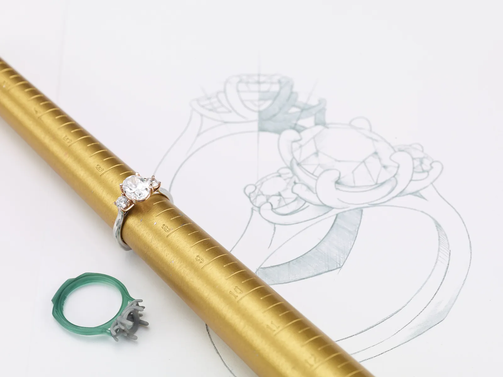 A diamond ring on a sizing tool with a ring sketch and a green wax model.