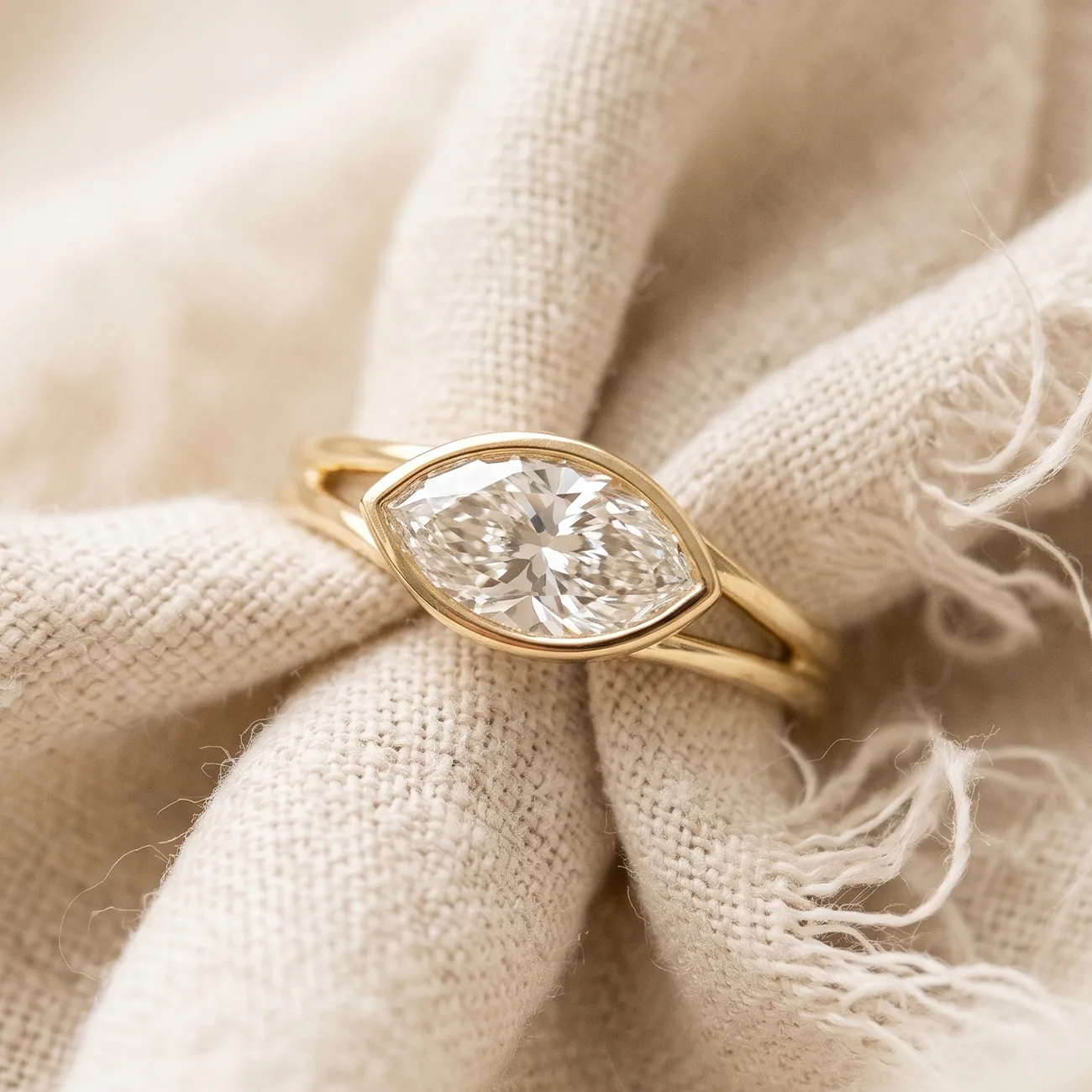 A marquise-cut diamond ring with a gold band on a textured fabric background.