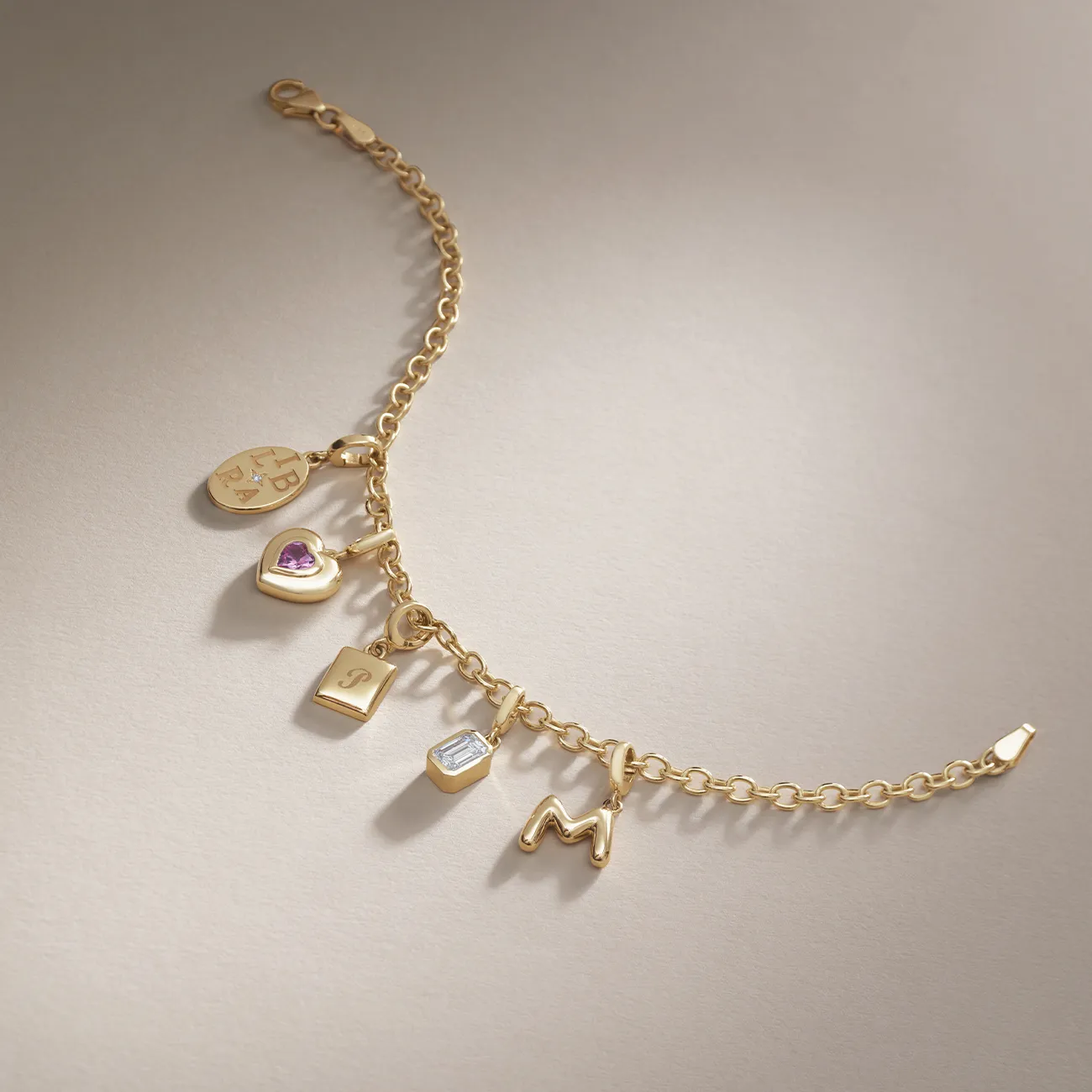 Gold charm bracelet with various pendants, including a heart and letter 