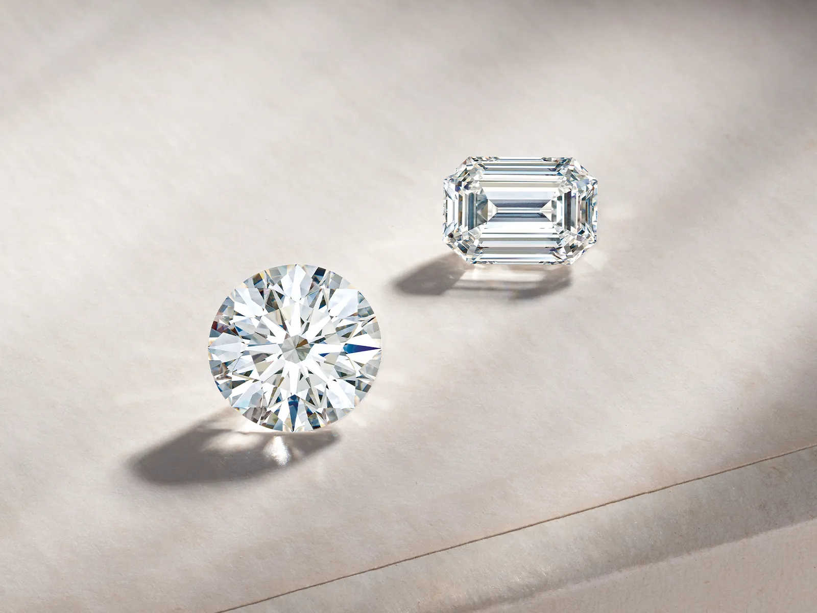 Two diamonds on a textured surface: one round brilliant cut, one emerald cut.