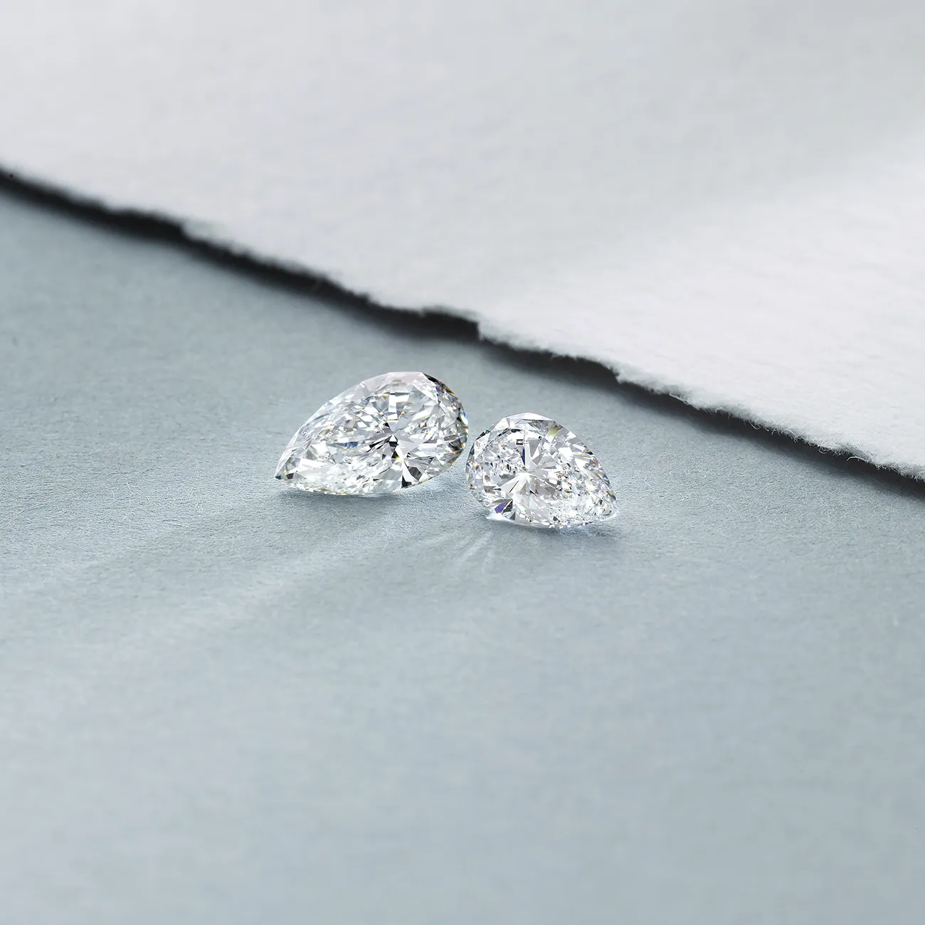 Two pear-shaped diamonds on a textured gray and white background.