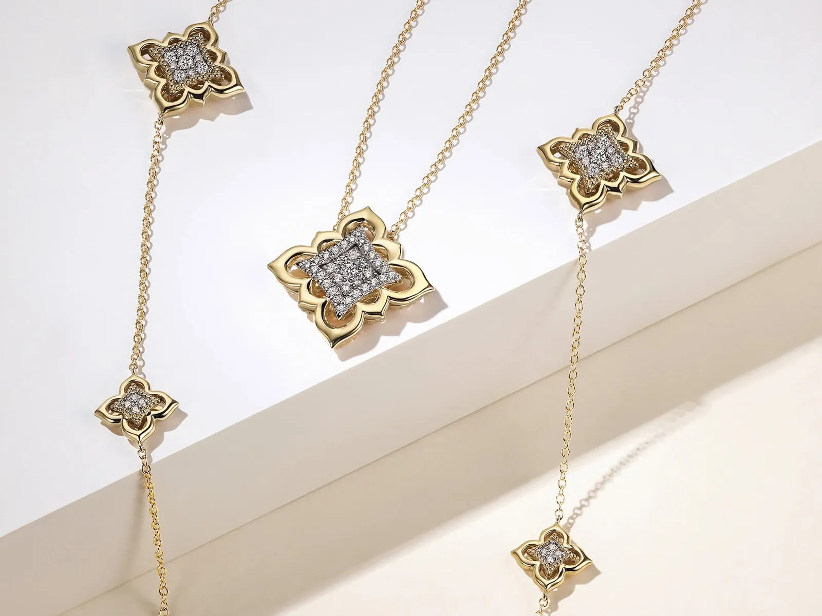 Gold necklace with diamond-studded floral pendants on a white background.