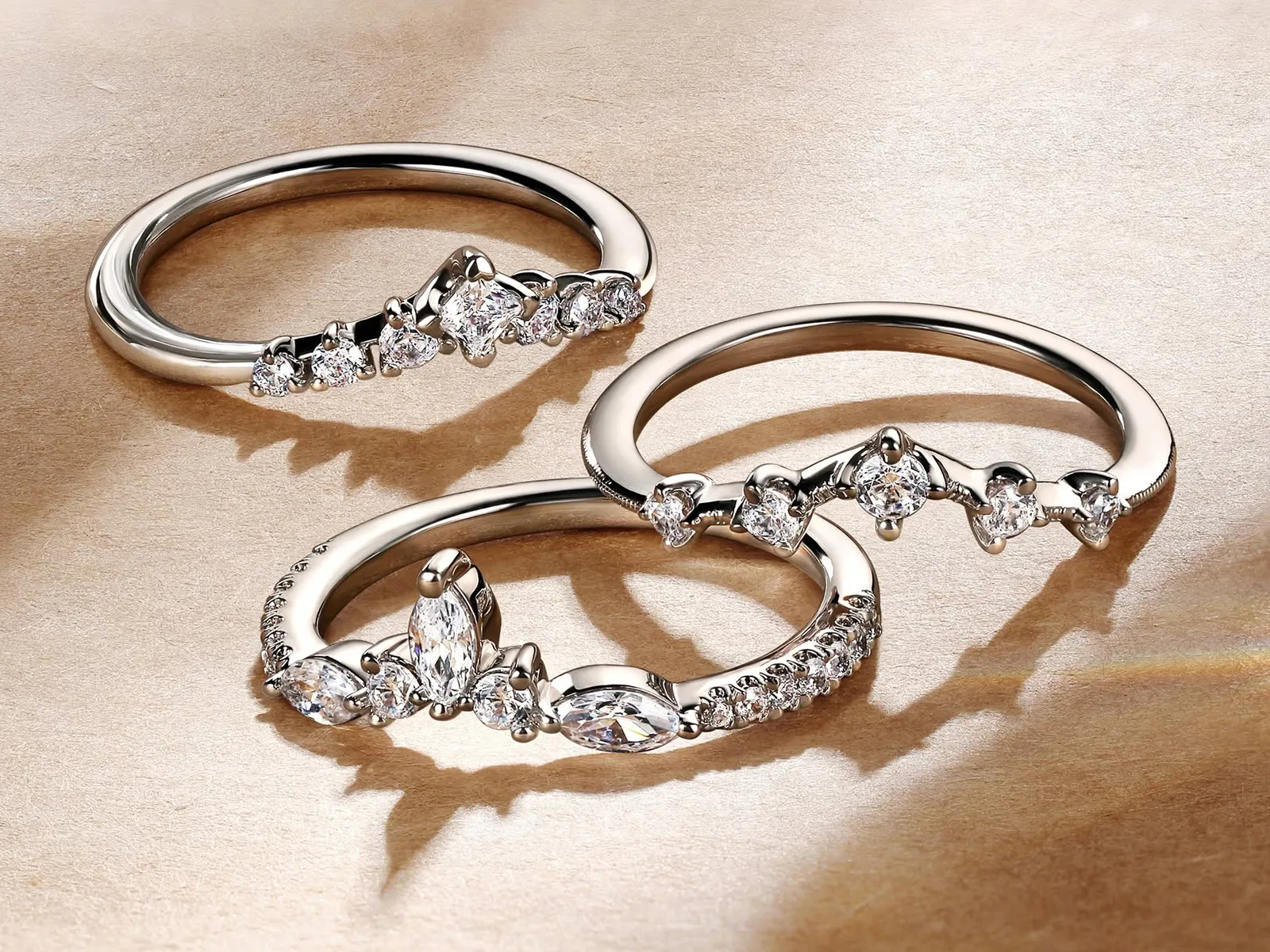 Three elegant diamond rings with intricate designs on a beige background.