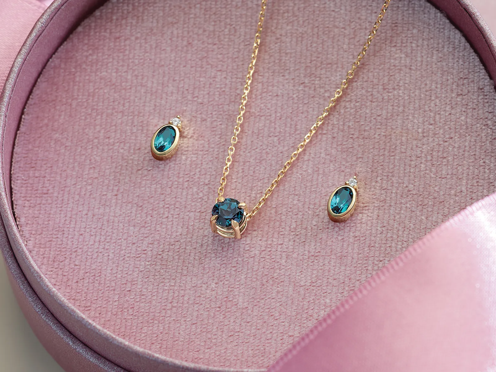 Gold necklace and earrings with blue gemstones in a pink jewelry box.
